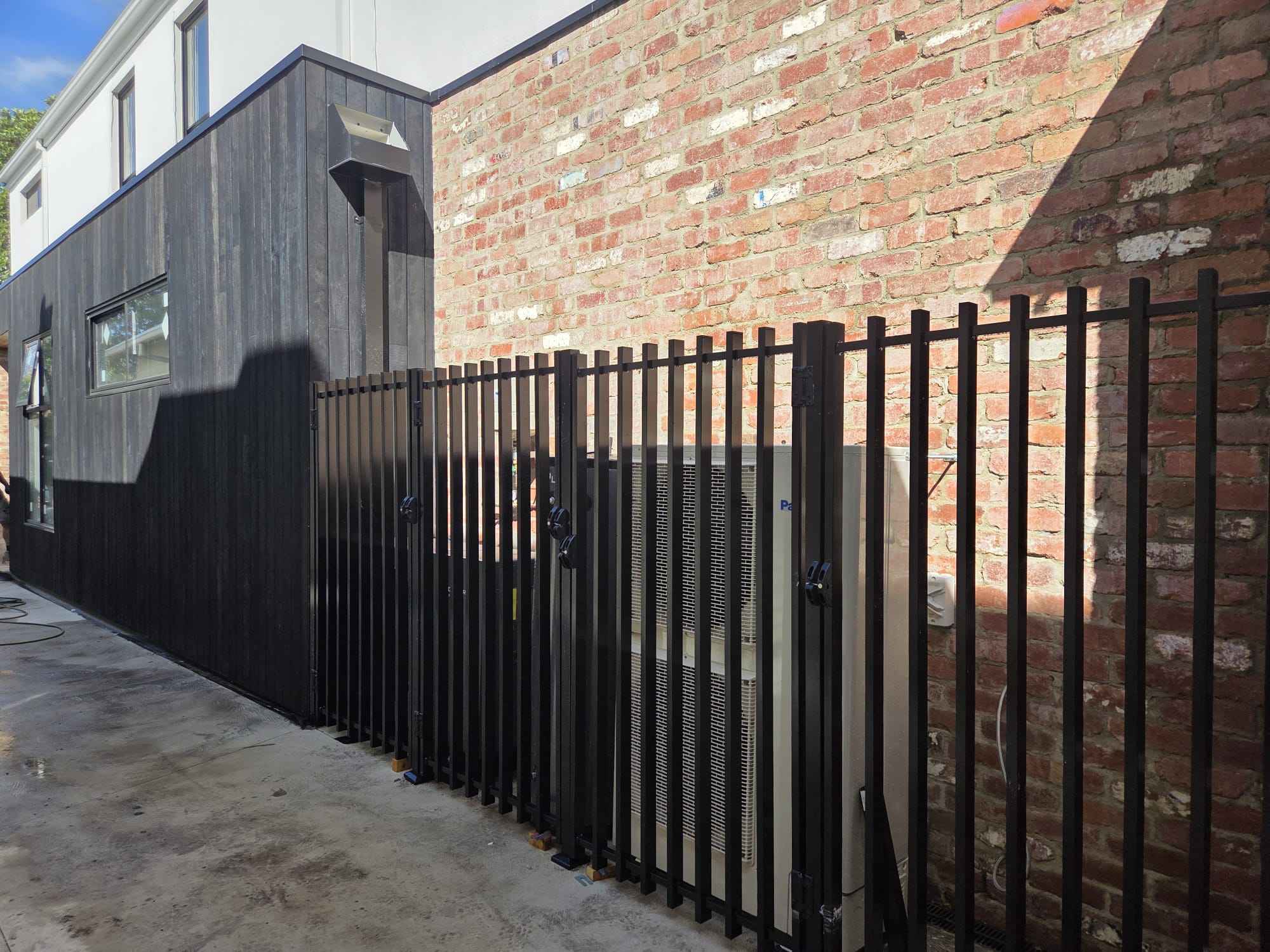 Black steel picket fence and gate beside a brick home